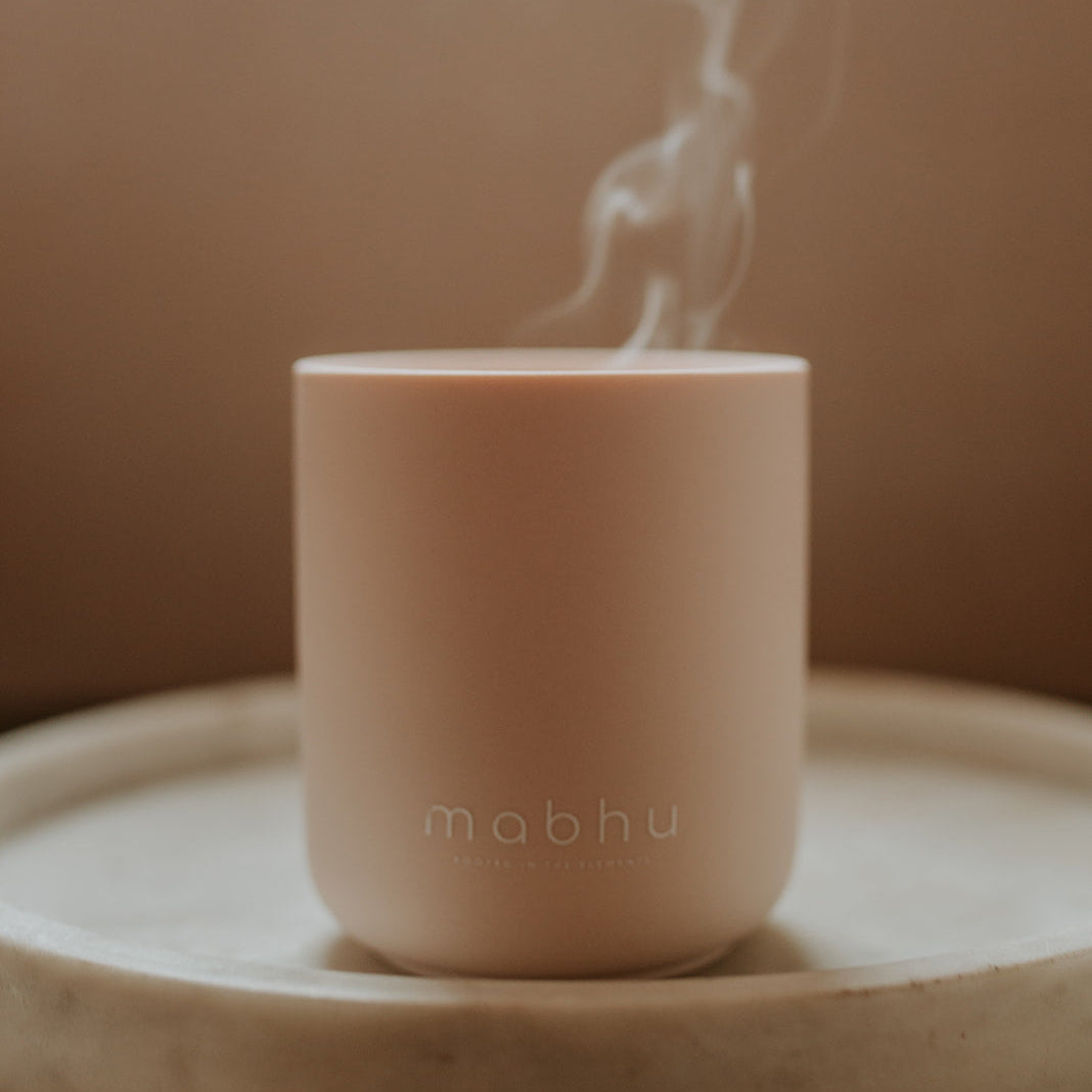 Pink ceramic cup with steam rising from it on a wooden surface against a brown background
